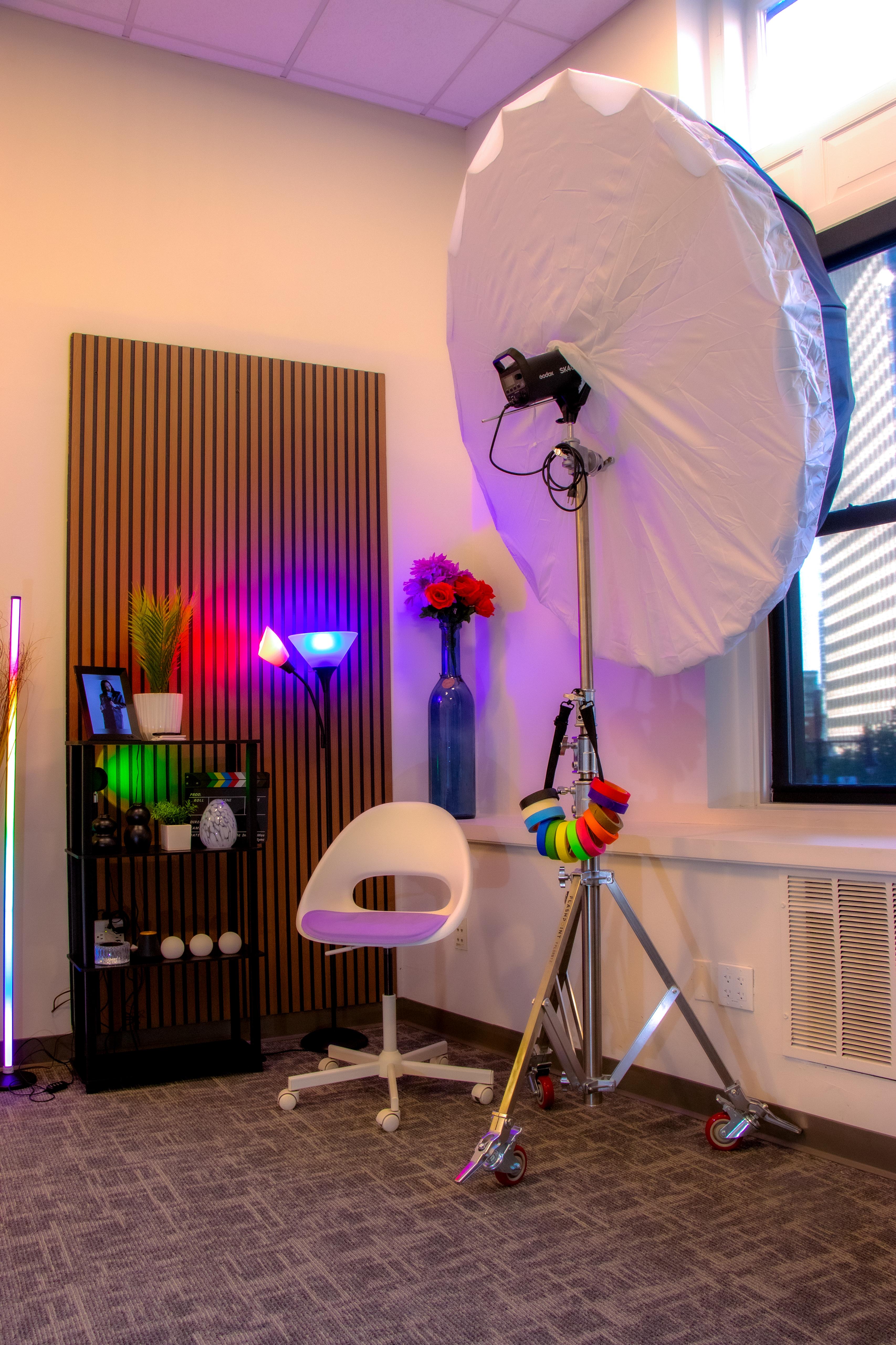 Styled creative set corner with a large parabolic light, white chair, and RGB-lit shelf