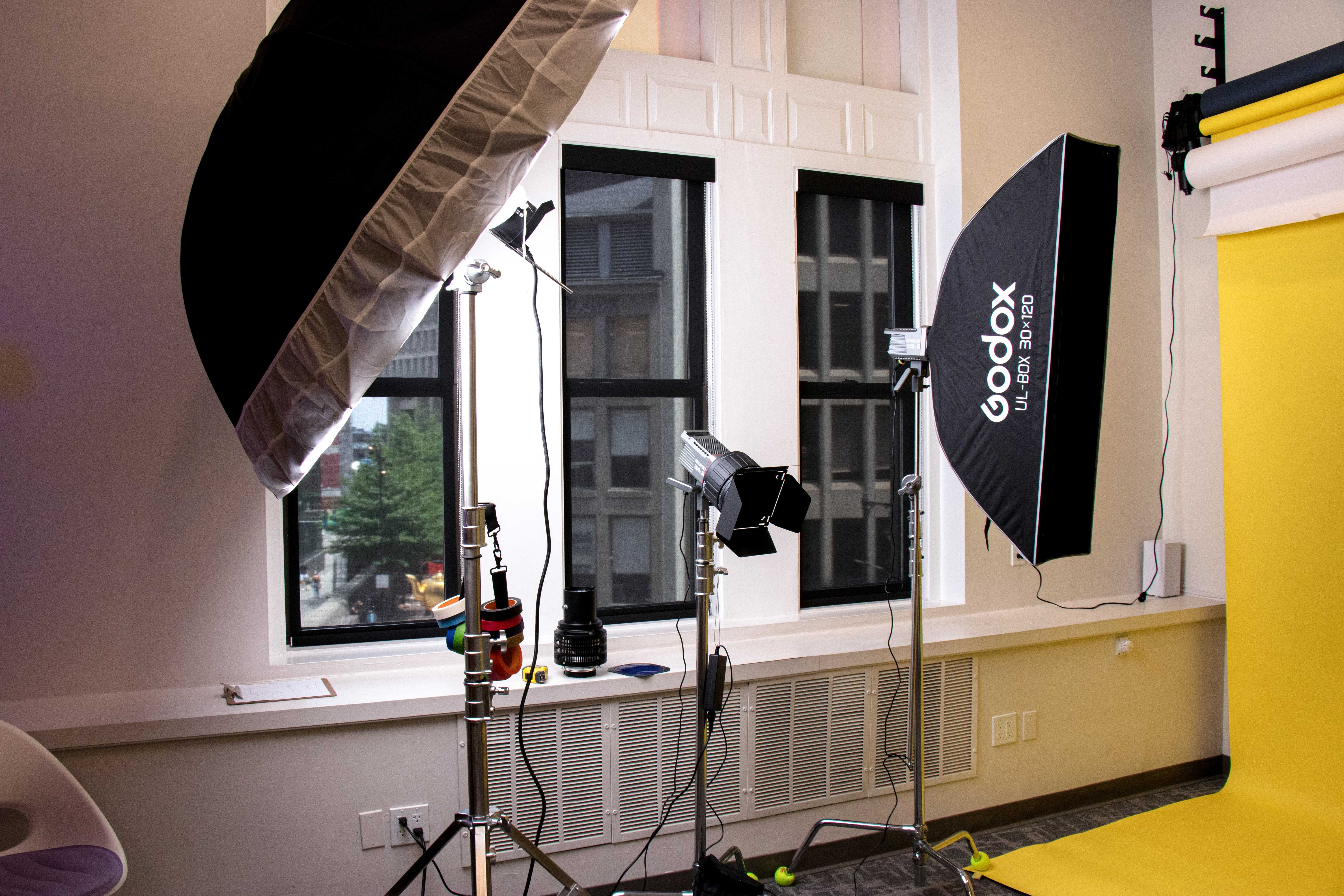 Studio lighting setup beside tall windows with a city view and yellow backdrop