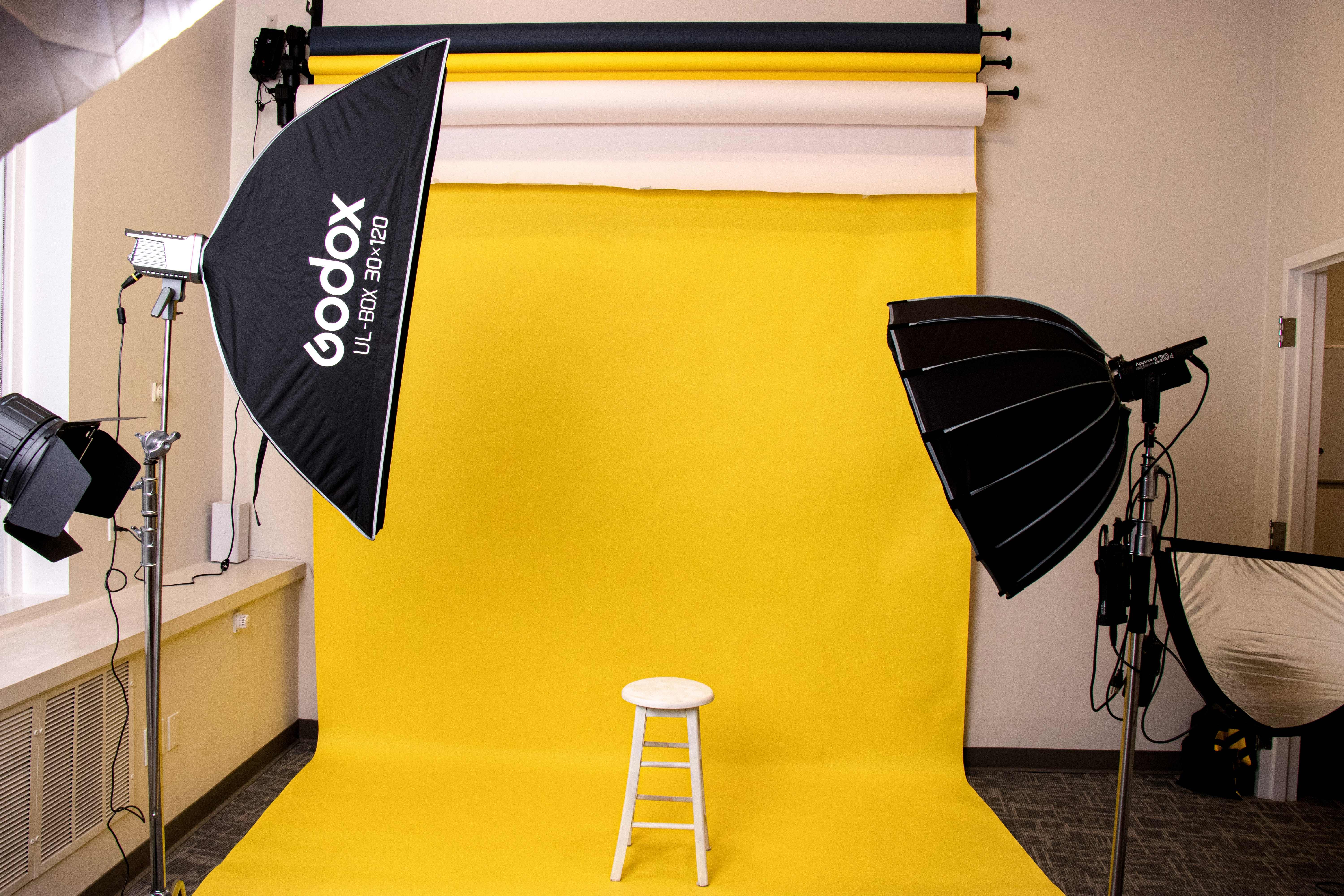 Bright yellow seamless backdrop with a white stool and studio lighting on both sides