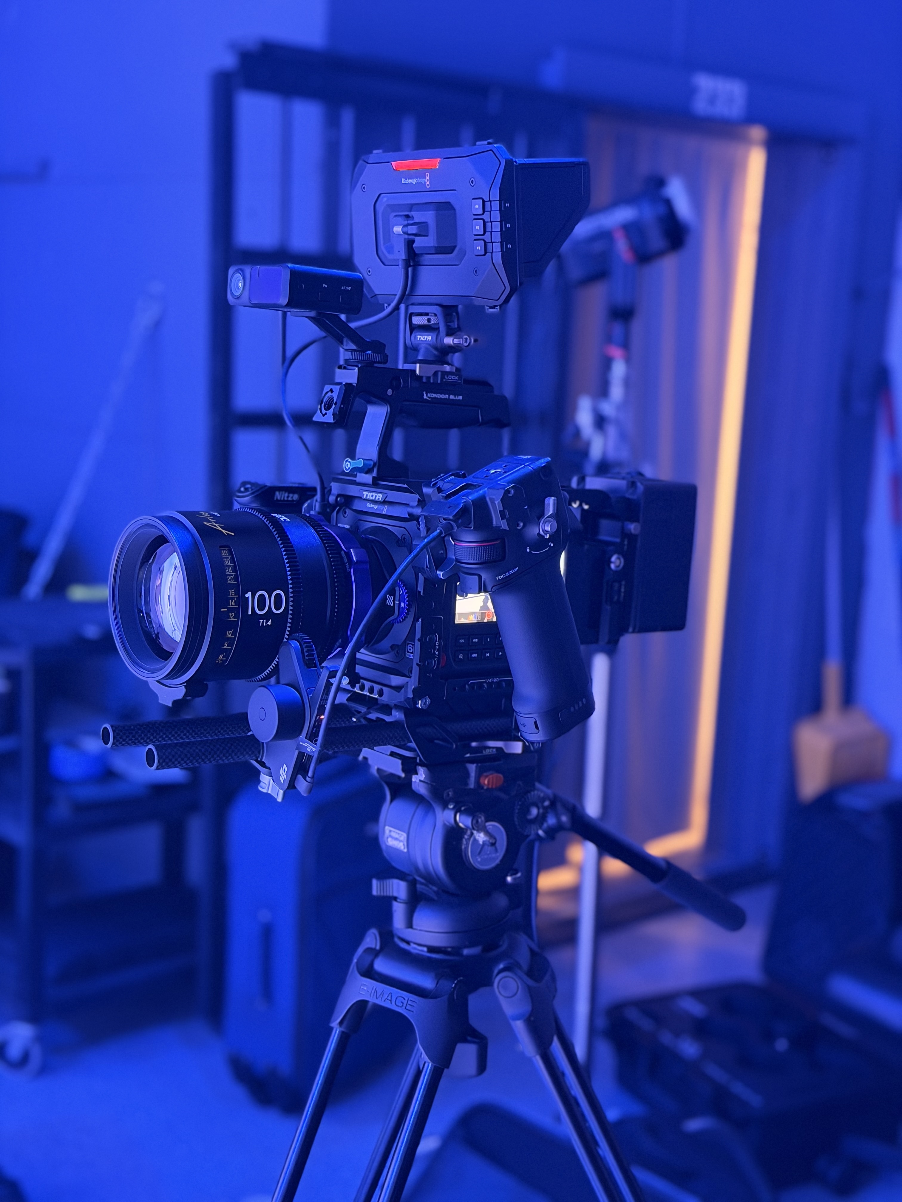 Close-up of a cinema camera rig with a 100mm lens on a tripod in blue light