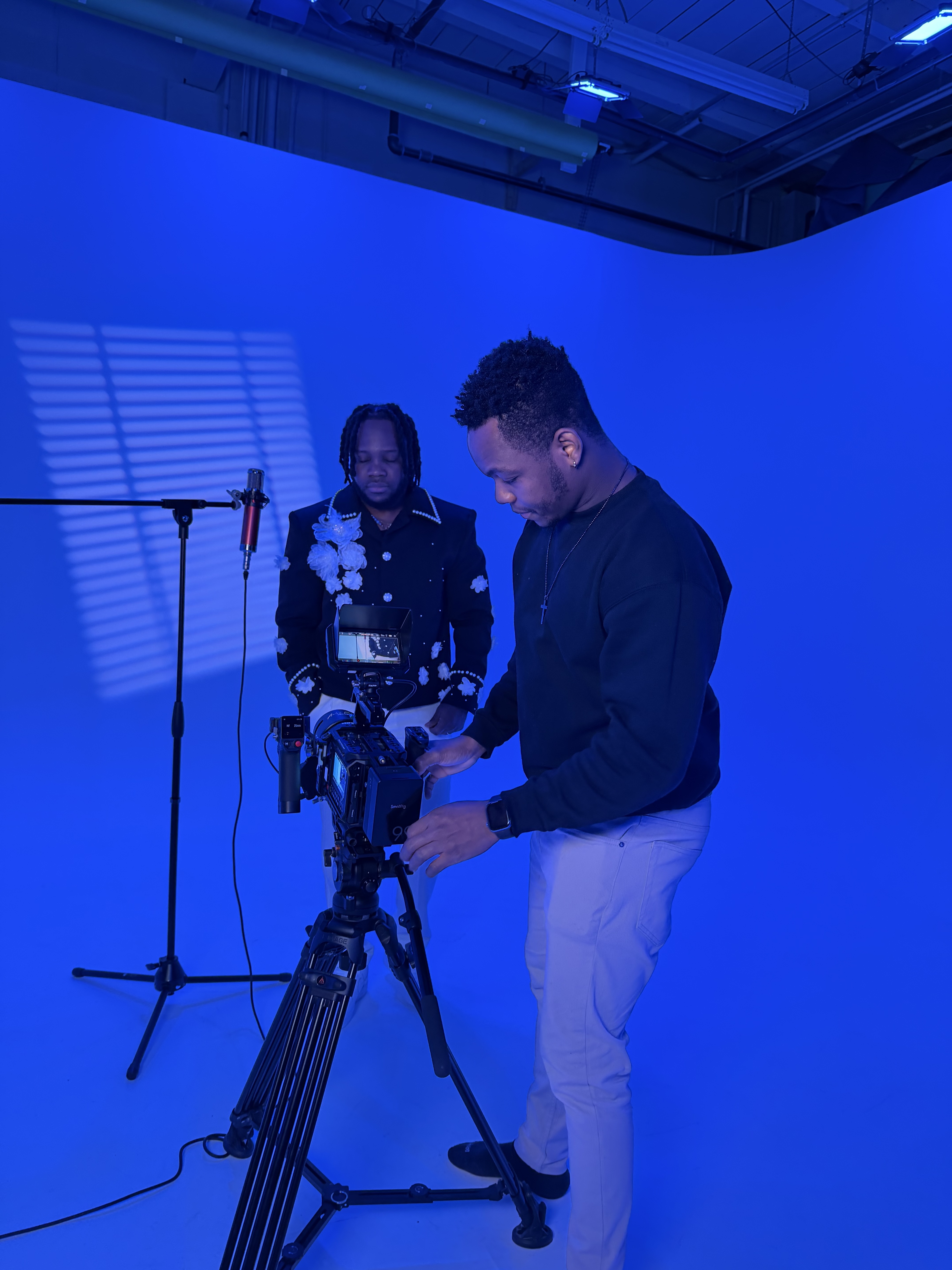 Two creators setting up a cinema camera for a podcast shoot on a blue-lit set